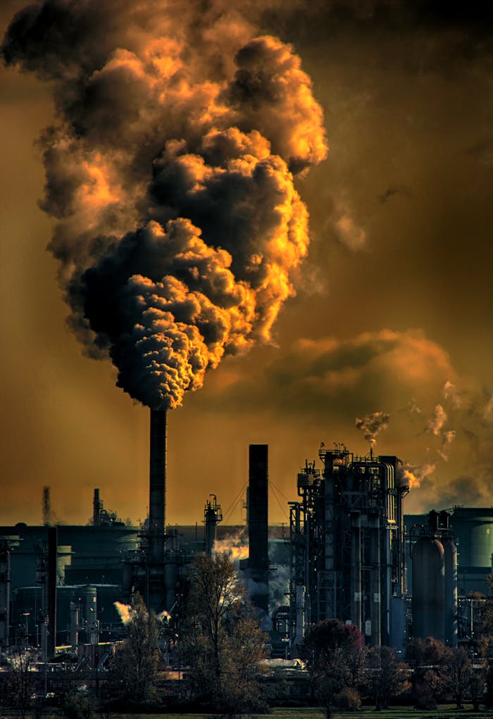 A factory emitting smoke clouds against a dark sunset sky, illustrating air pollution and industrial impact.